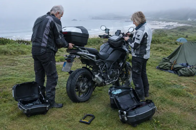 Sur un camping breton noyé de brume, un couple de motards fixe le top case et prépare les valises latérales de sa routière avant de reprendre la route