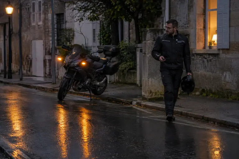 La nuit sous la bruine, un motard active l’alarme de sa moto routière avec une télécommande, les clignotants s’allument dans une rue de Bordeaux