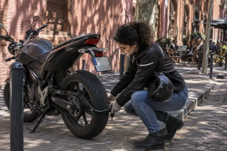 Une jeune motarde ferme un antivol U passé dans la jante arrière et le bras oscillant de sa moto, dans une rue de briques roses à Toulouse