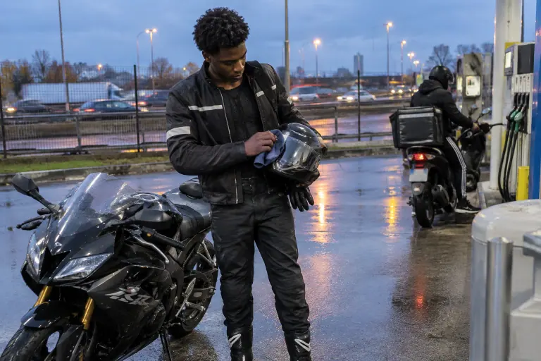 À l’aube dans une station-service près du périphérique parisien, un jeune motard essuie la visière de son casque à côté de sa petite sportive 125