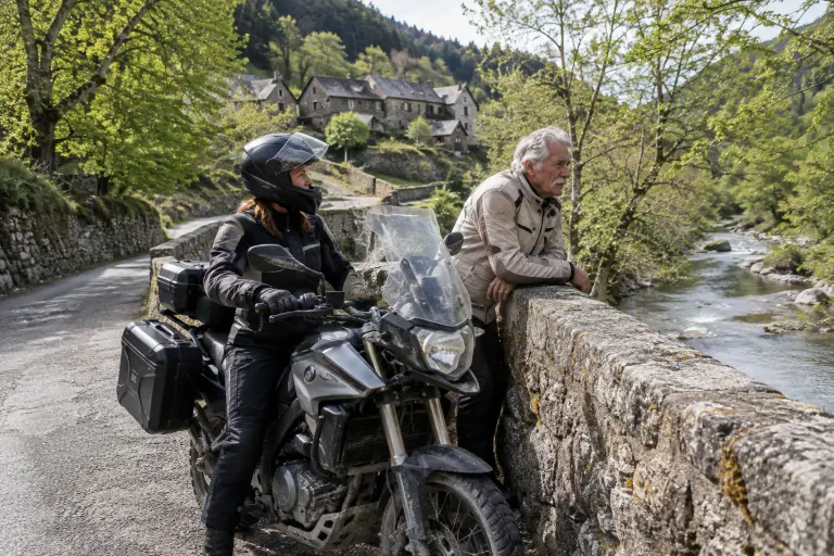 Sur un vieux pont de pierre des Cévennes, un père et sa fille font une pause près d’un trail bicylindre de moyenne cylindrée équipé de valises