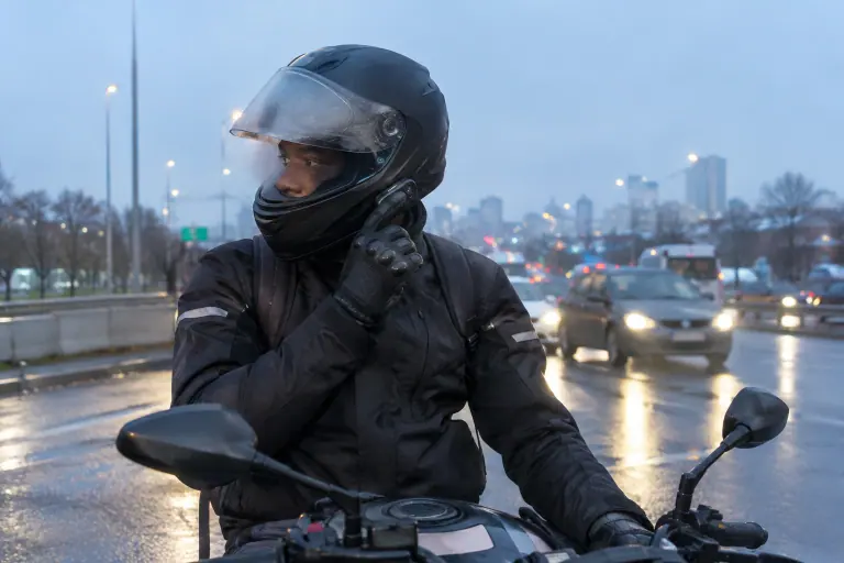Au petit matin près du périphérique, un motard arrêté au feu appuie du pouce sur la commande bluetooth intégrée à son casque modulable