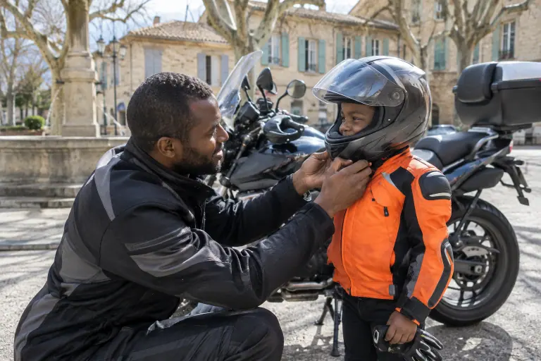 Sur une place de village de la Drôme, un père vérifie que le casque intégral de son fils de huit ans ne tourne pas, avant une balade à moto