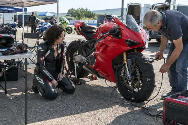 Dans le paddock d’un circuit du Gard, une pilote en combinaison cuir prépare sa sportive rouge à monobras équipée de couvertures chauffantes