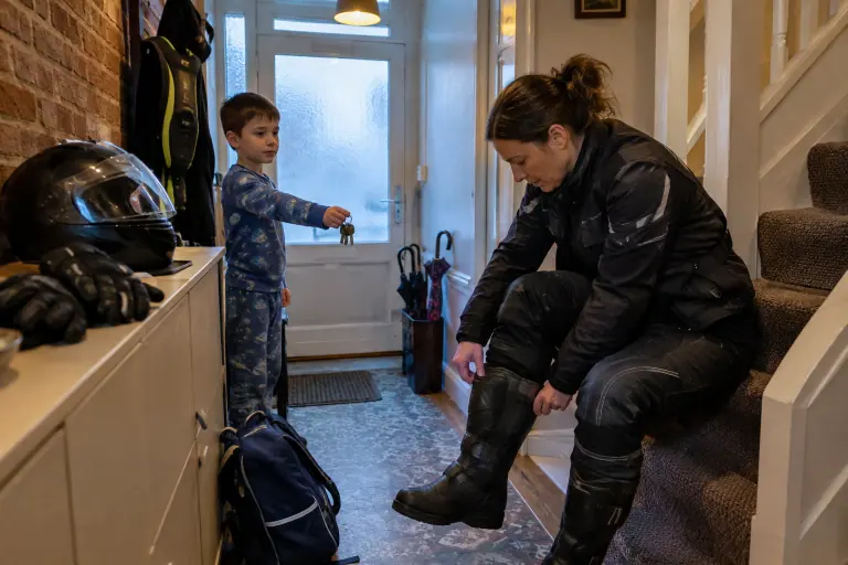 Dans l’entrée d’une maison lilloise, une motarde enfile ses bottes avant le trajet du matin, casque intégral, gants et gilet airbag prêts à côté