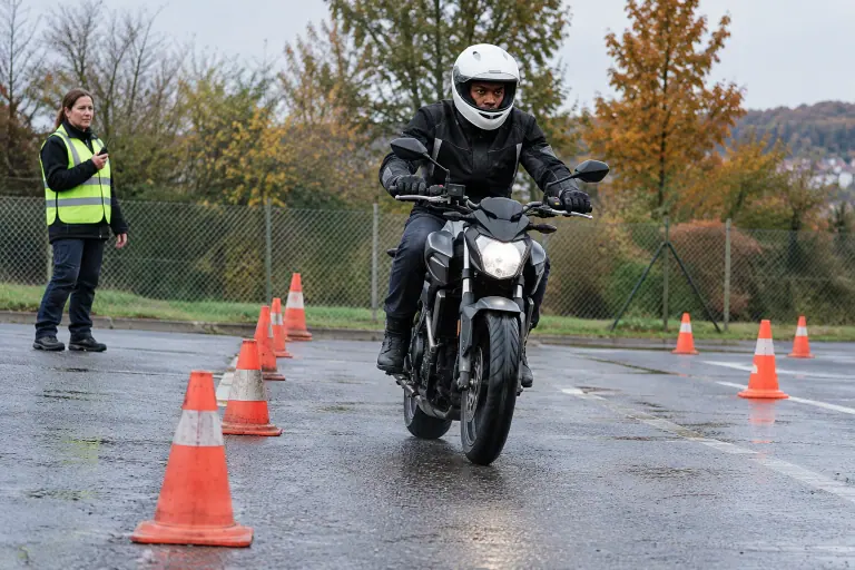 Sur l’aire d’entraînement d’une moto-école, un jeune motard réalise un freinage d’urgence entre des plots, sous le regard de sa monitrice