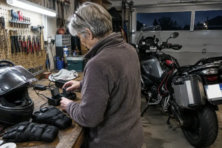 Dans son garage, une motarde d’une soixantaine d’années met en charge les batteries de ses gants chauffants sur l’établi, sa routière garée derrière elle