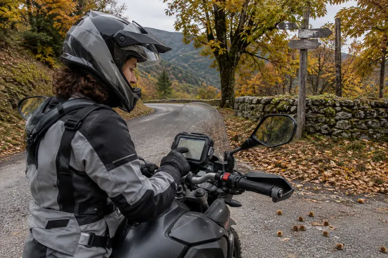 Une motarde arrêtée à une intersection d’une petite route des Cévennes touche du gant l’écran du GPS fixé sur le guidon de son trail