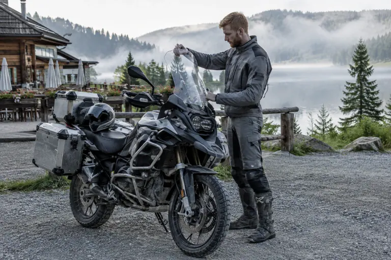 Au petit matin sur le parking d’une auberge au bord d’un lac du Jura, un motard très grand règle la hauteur de la bulle de son gros trail équipé de valises