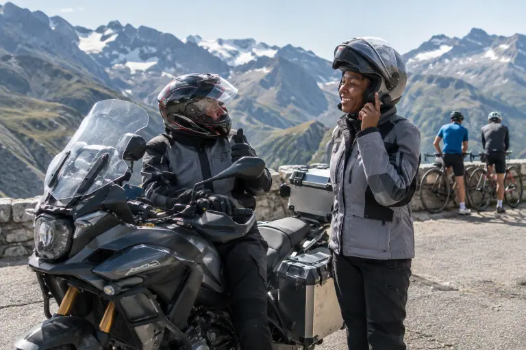 Au sommet d’un col alpin, une passagère règle l’intercom fixé sur son casque modulable à côté d’un gros trail équipé de valises en aluminium