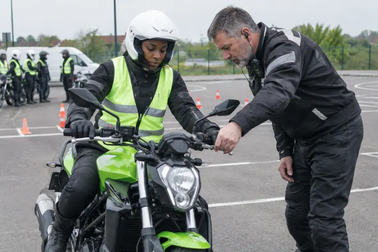 Sur la piste d’une moto-école près de Lille, un moniteur règle le levier d’embrayage d’une élève assise sur un roadster vert en gilet jaune