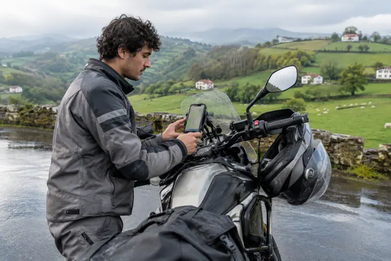 Au Pays basque après la pluie, un jeune motard ajuste son smartphone dans un support de guidon à amortisseur sur son trail avant de repartir