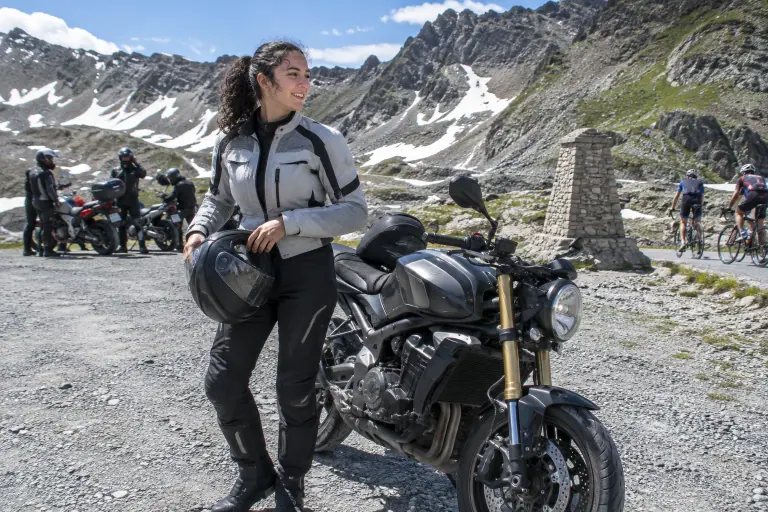 Une jeune motarde vient d’ôter son casque intégral à côté de son roadster bicylindre de moyenne cylindrée, garé au sommet d’un col alpin en plein été