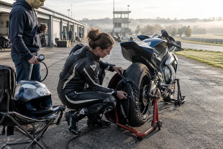 Dans le paddock d’un petit circuit, une motarde en combinaison cuir retire les couvertures chauffantes d’une moto sportive carénée posée sur béquilles