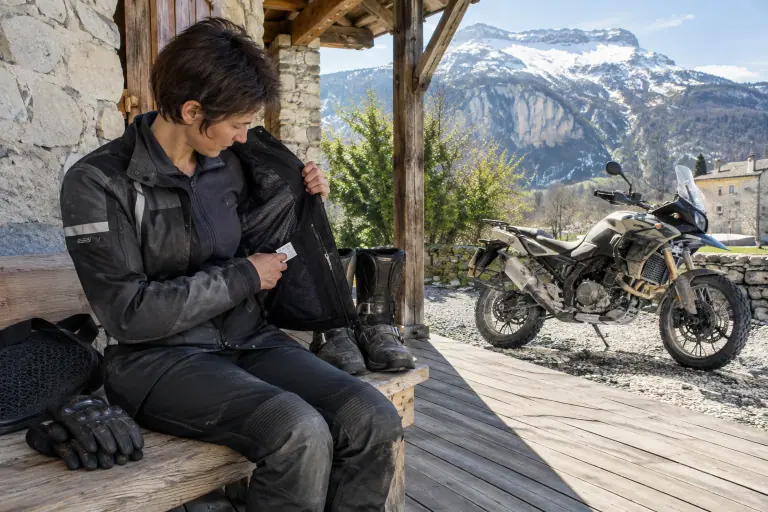 Sur le perron d’une ferme du Vercors, une motarde lit l’étiquette cousue dans son blouson textile, gants, bottes et dorsale posés à côté d’elle