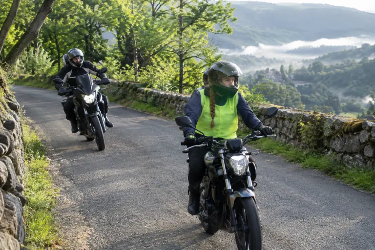 Sur une petite route des Cévennes, une lycéenne équipée d’un gilet fluo conduit une moto 125 d’école, suivie de près par son moniteur à moto
