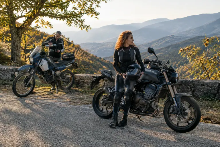 Sur une petite route des Cévennes en automne, une jeune motarde récemment titulaire du permis fait une pause près de sa moto, casque à la main