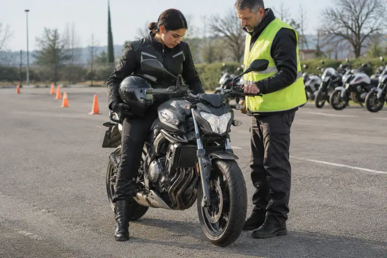 Une jeune motarde équipée, assise sur un roadster sur le parking d’une moto-école, vérifie qu’elle pose bien les deux pieds au sol près de son moniteur