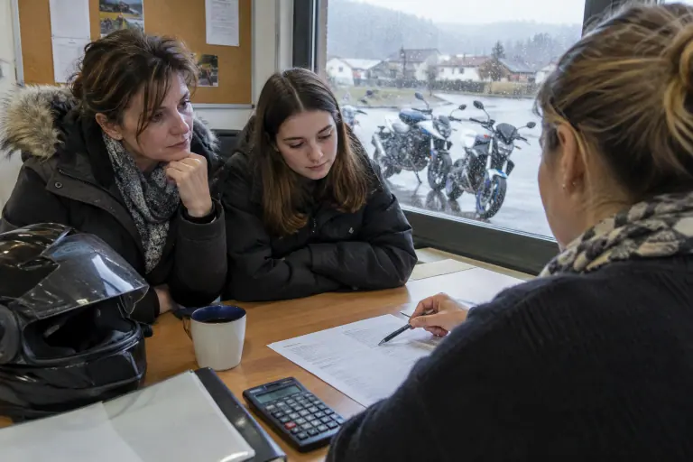 Dans le bureau d’une moto-école en Auvergne, une mère et sa fille de dix-huit ans étudient un devis de permis moto avec la monitrice