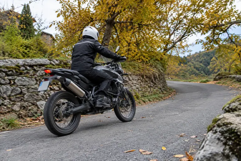 Un jeune motard roule calmement sur un trail neuf aux pneus encore brillants, dans un virage bordé de murets et de châtaigniers des Cévennes en automne