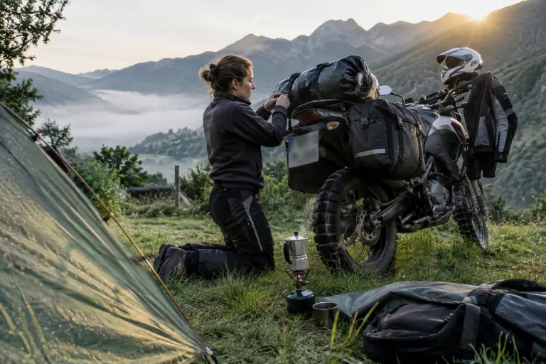 À l’aube dans un camping des Pyrénées ariégeoises, une jeune motarde sangle un sac étanche sur son trail équipé de sacoches latérales souples
